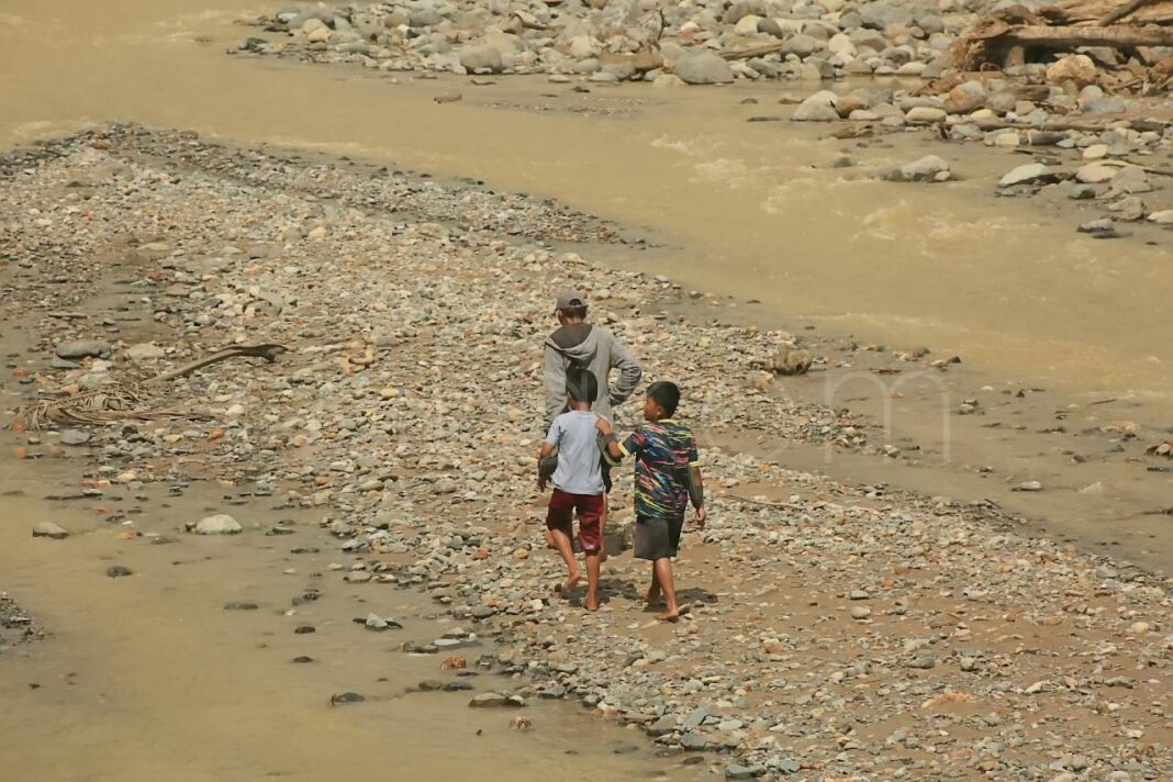 Warga Kelurahan Lambung Bukit menyeberangi sungai Batu Busuk Padang.
